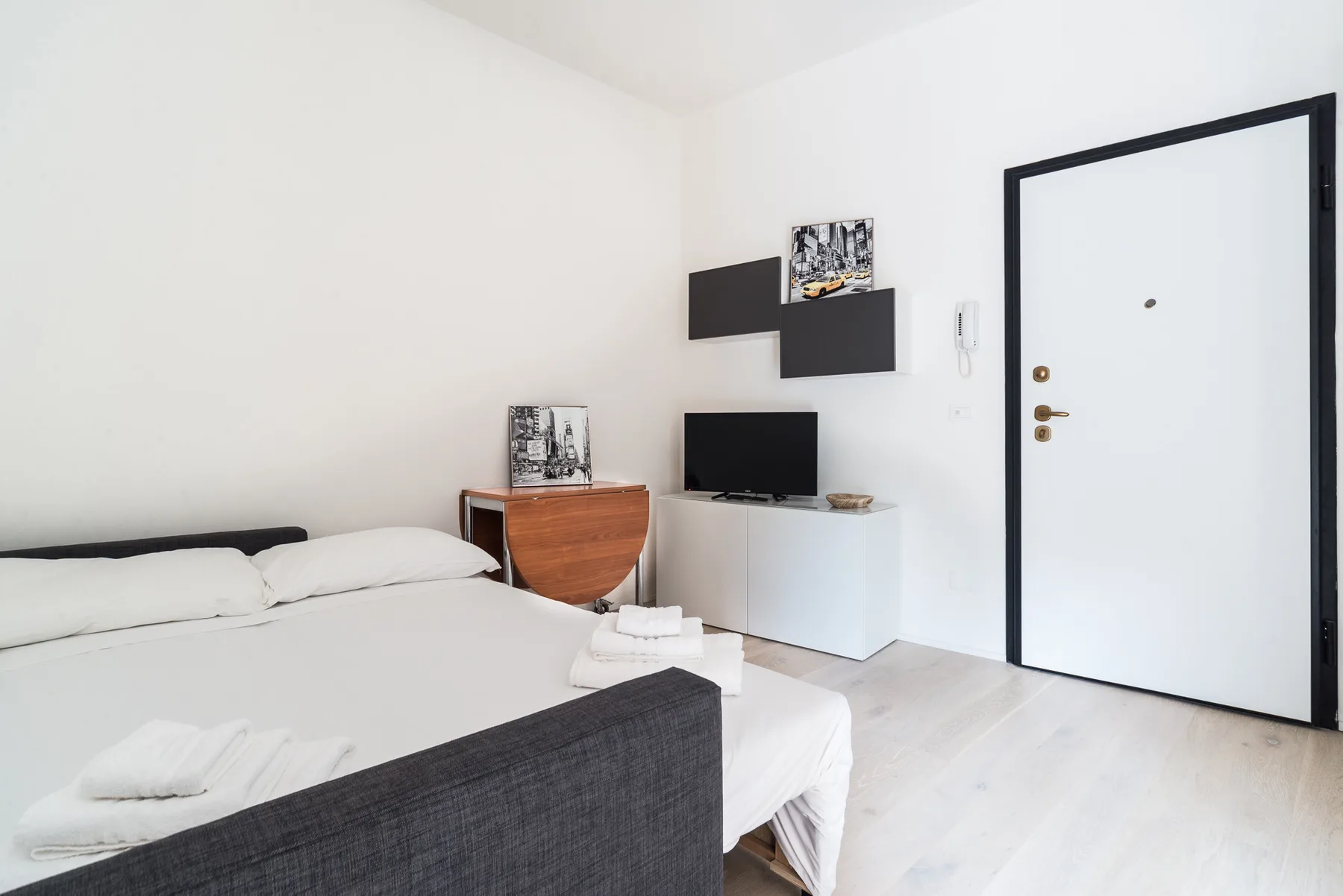 Un dormitorio luminoso con una cama, un televisor y una puerta blanca de entrada.