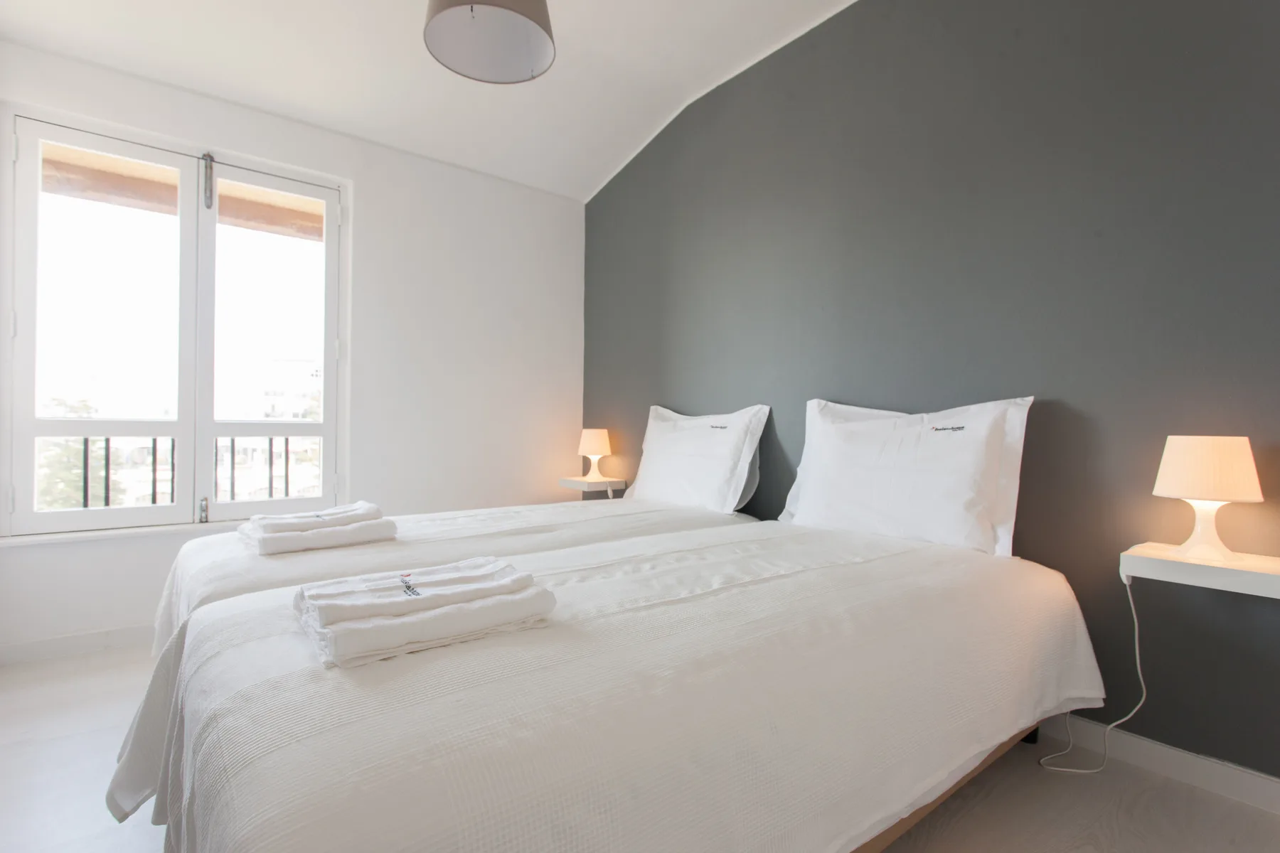 A bedroom with a neatly made bed and tall windows.