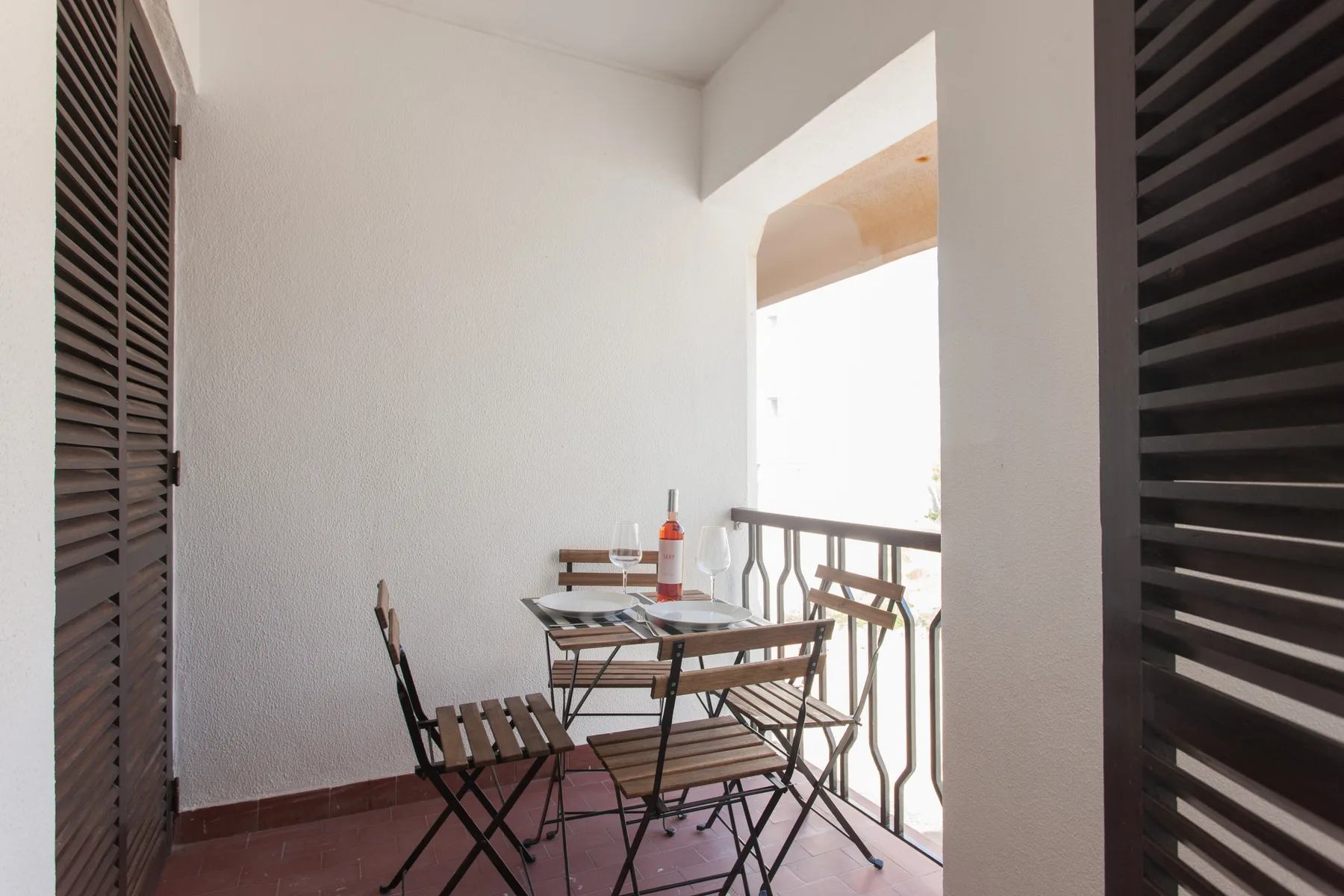 A small balcony has a folding table and chairs beside the railing.