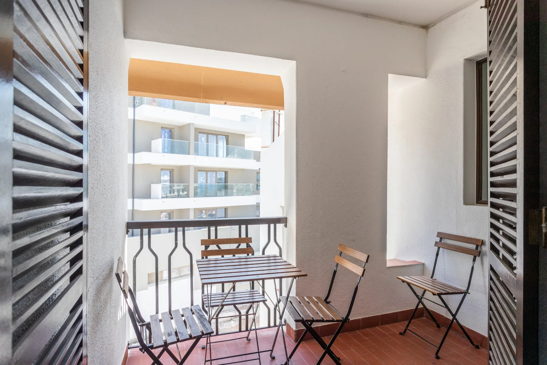 A small balcony with folding seating overlooks a neighboring apartment building.