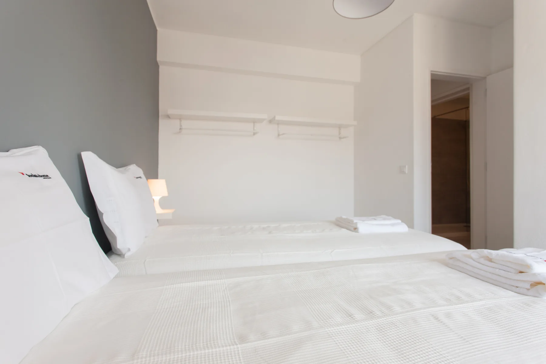 A bedroom with white bedding and a doorway opening into the adjoining space.