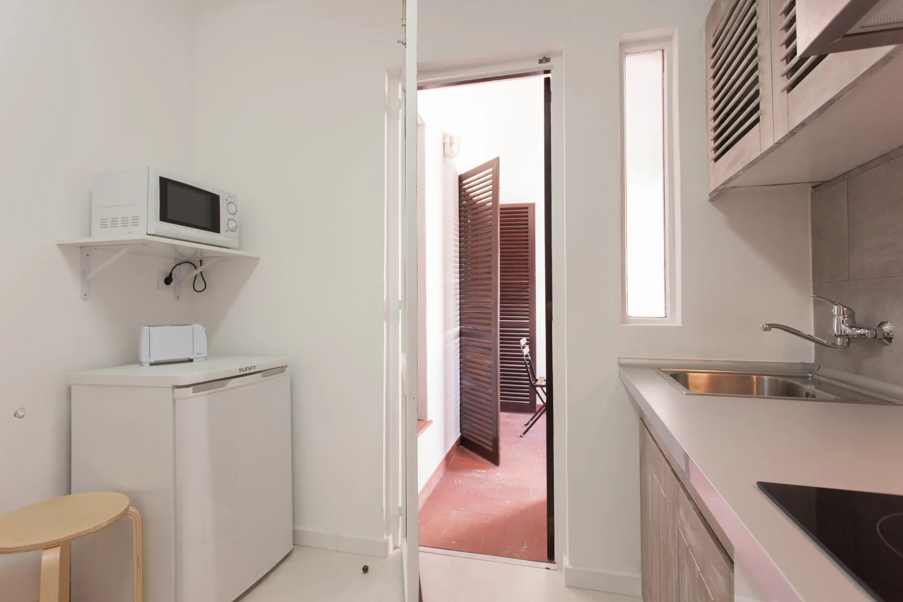 A compact kitchen with a counter, cooktop, and small appliances beside an open doorway.