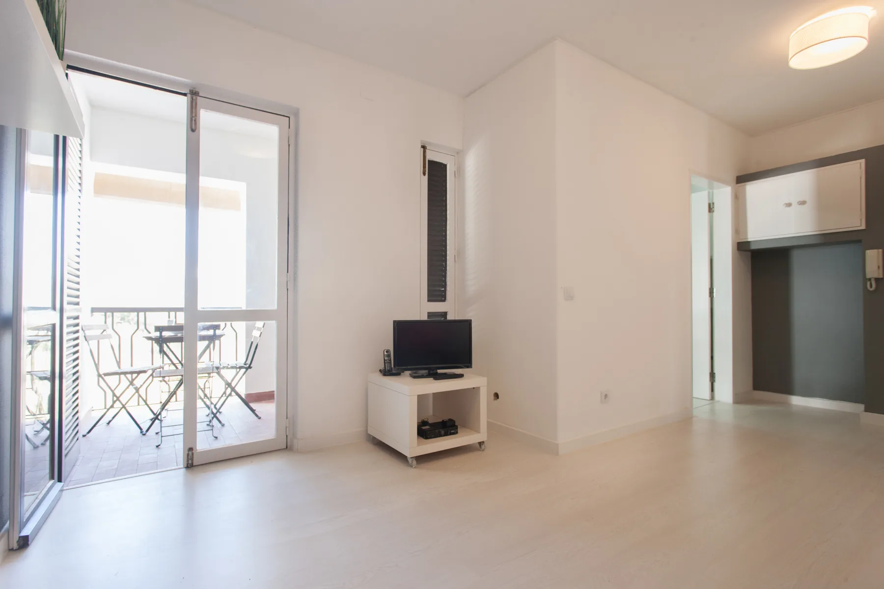 A bright living area with a television stand beside sliding glass doors to a balcony.