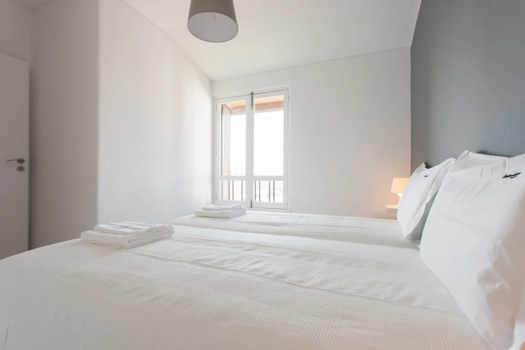 A bright bedroom with white bedding and a window.