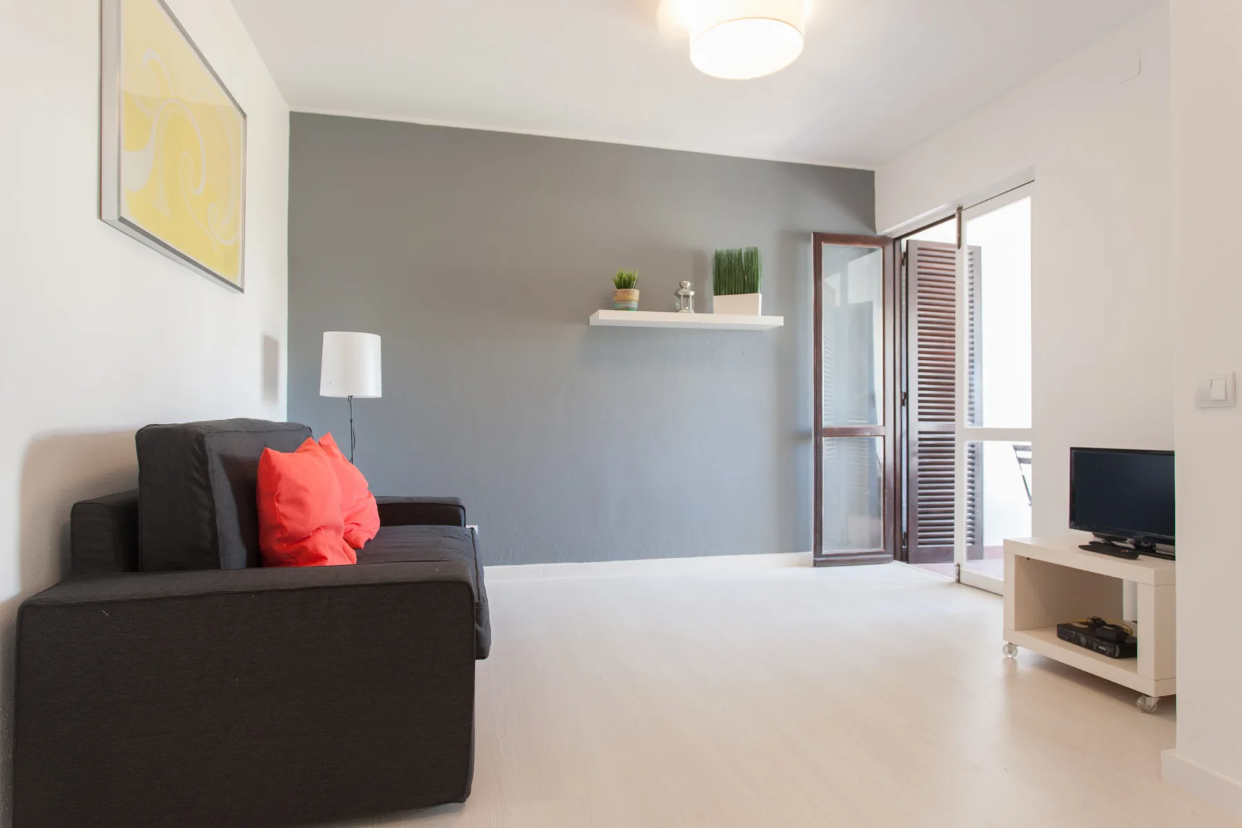 A living room with dark seating, a television, and an open balcony door.