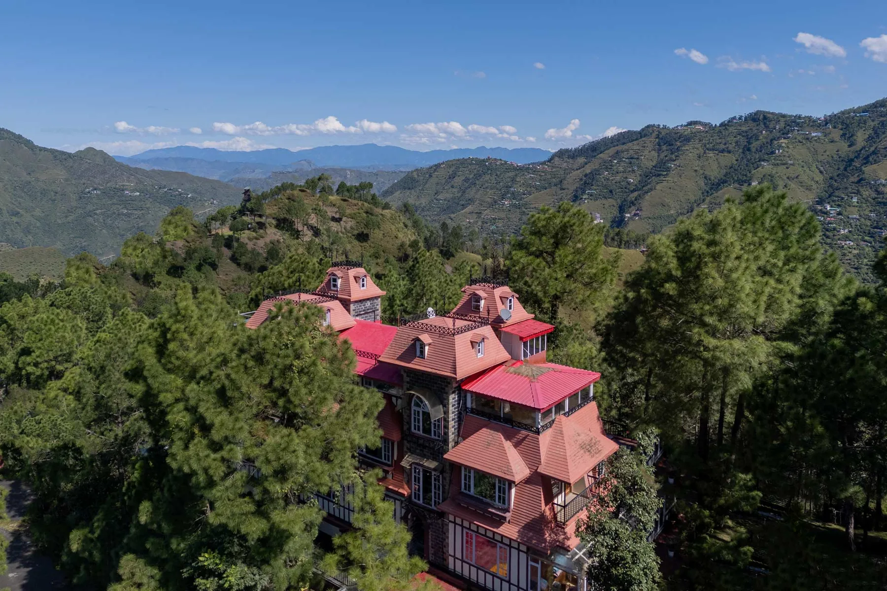 Una casa de techo rojo está entre árboles, con montañas al fondo.