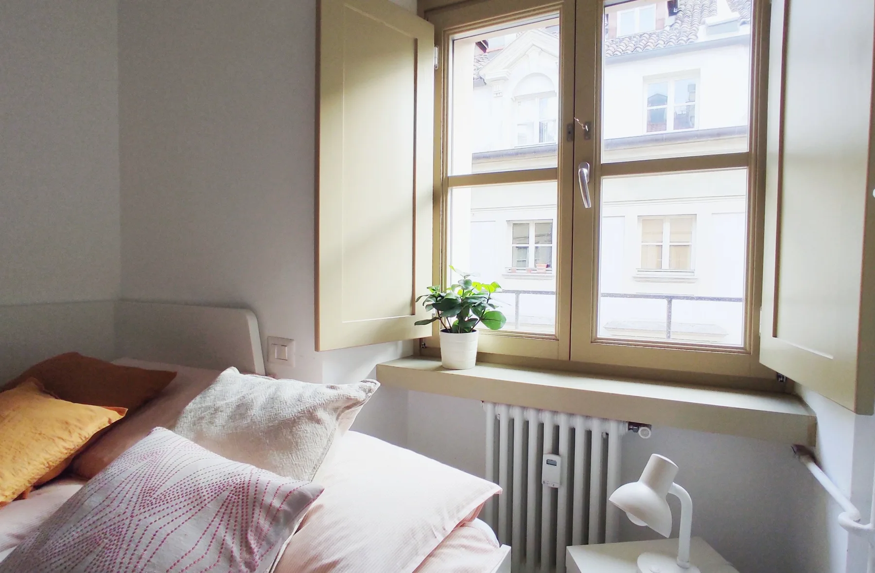 A bright bedroom with a bed beside a large window and potted plant.