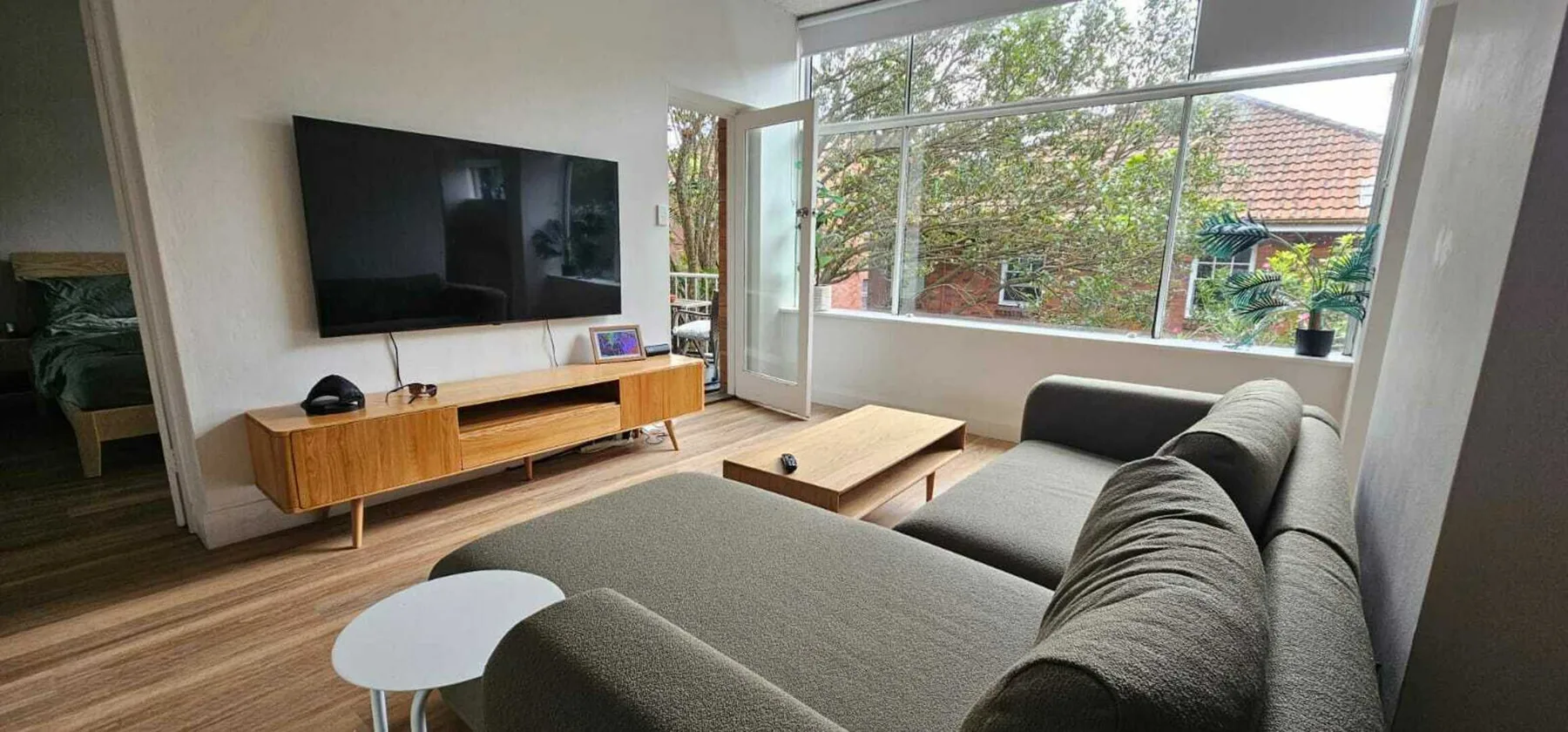 Una sala de estar con asientos grises, una mesa de centro y ventanas grandes.