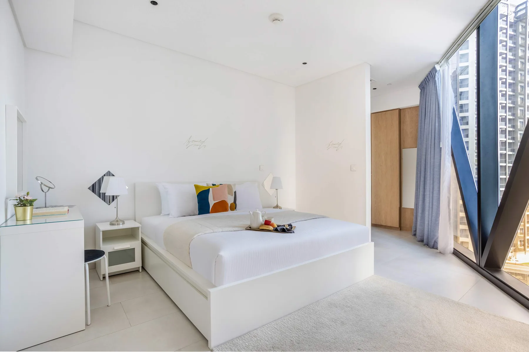 A bright bedroom with a neatly made bed beside floor-to-ceiling windows.