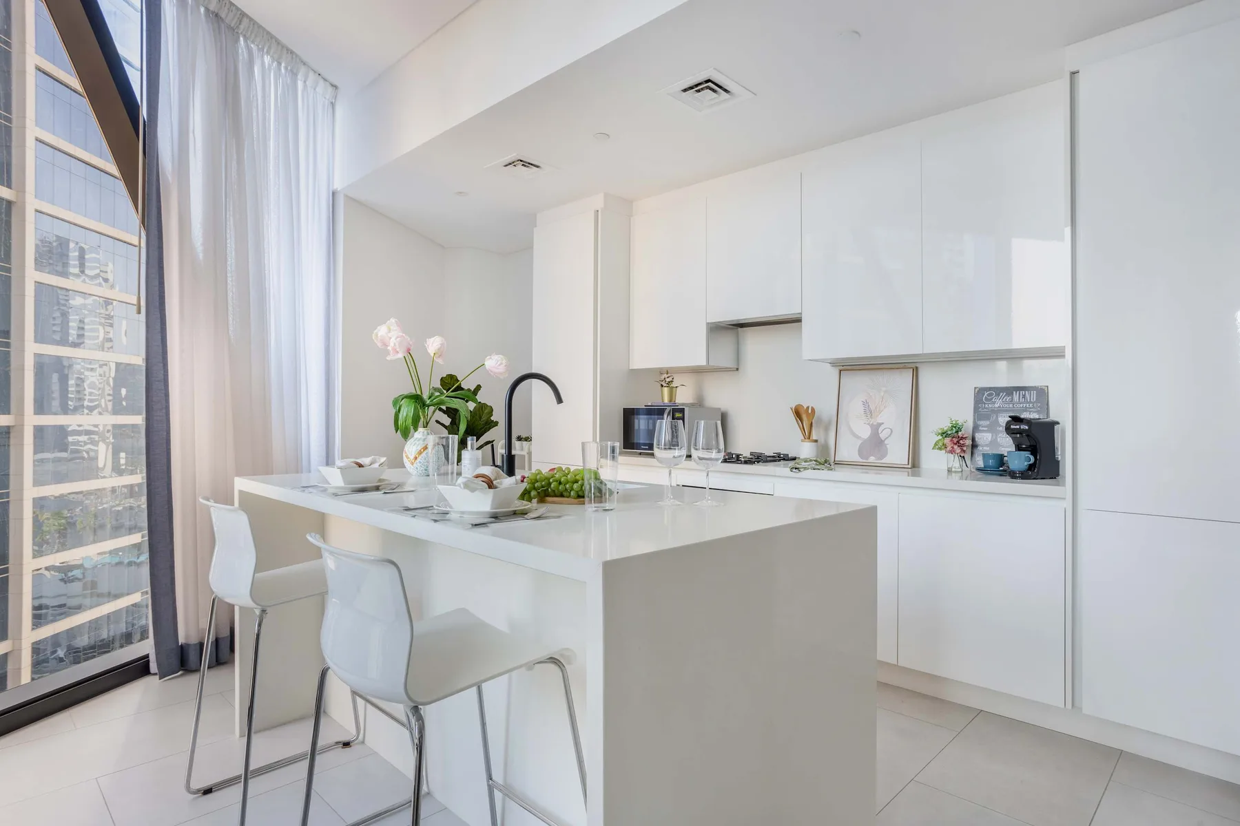 A bright modern kitchen with a white island and large windows.