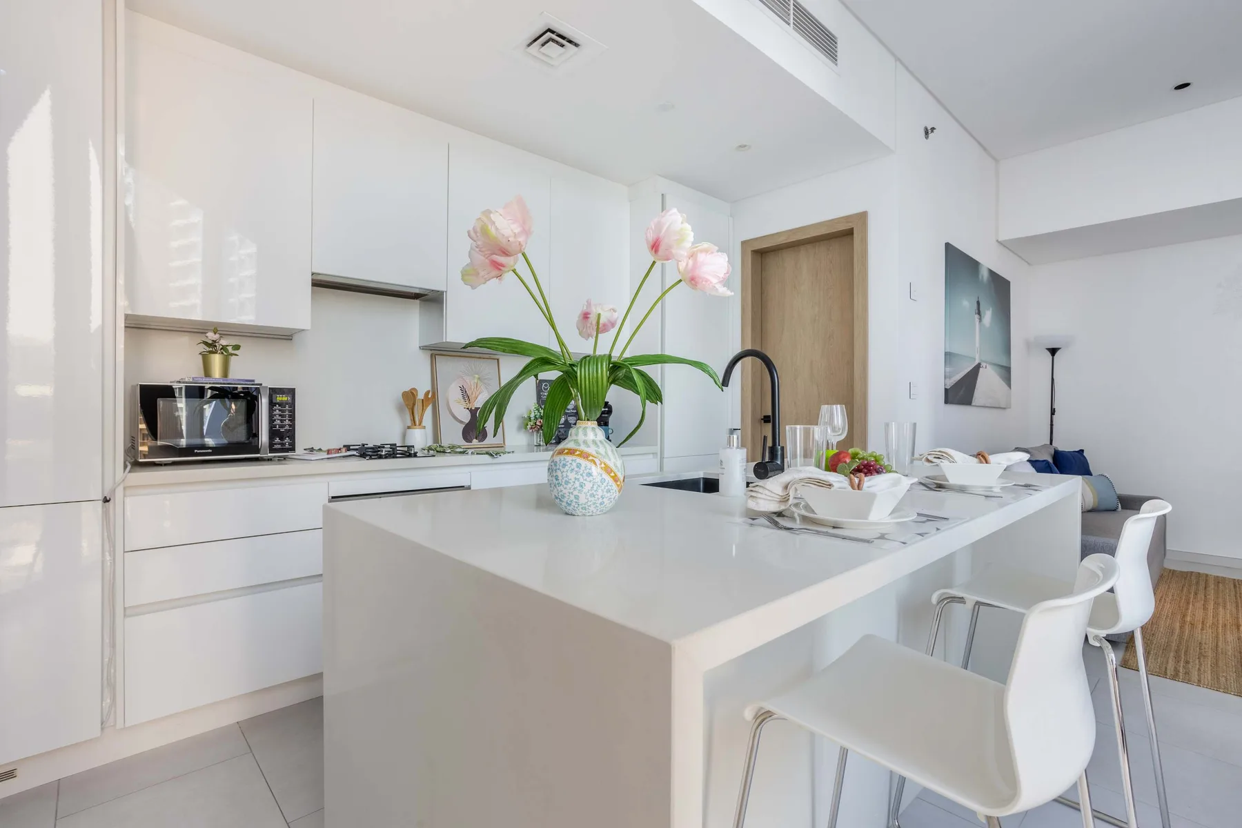 A bright modern kitchen with a white island and flowers in a vase.