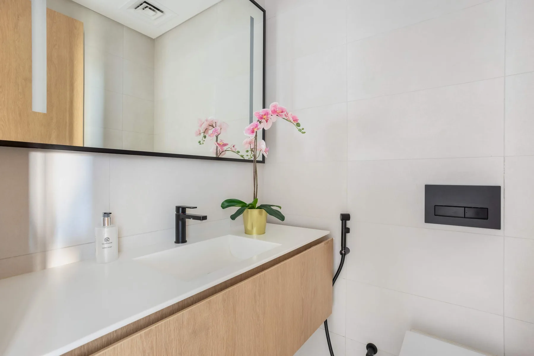 A bright bathroom with a white vanity, wall-mounted faucet, and pink orchid.