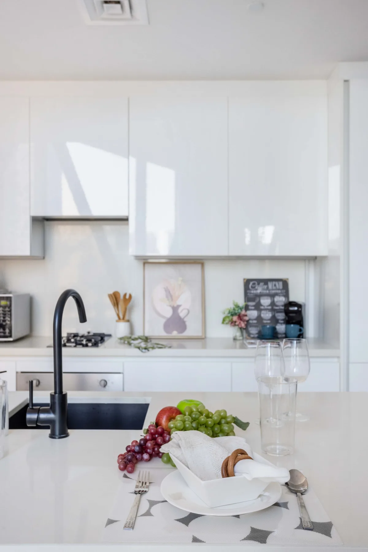 A bright kitchen with white cabinets, a dark faucet, and a dining place setting on the island.
