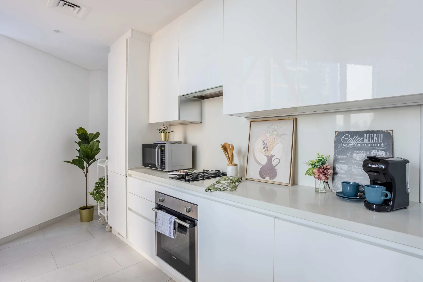 A bright modern kitchen with white cabinetry, a cooktop, and countertop decor.