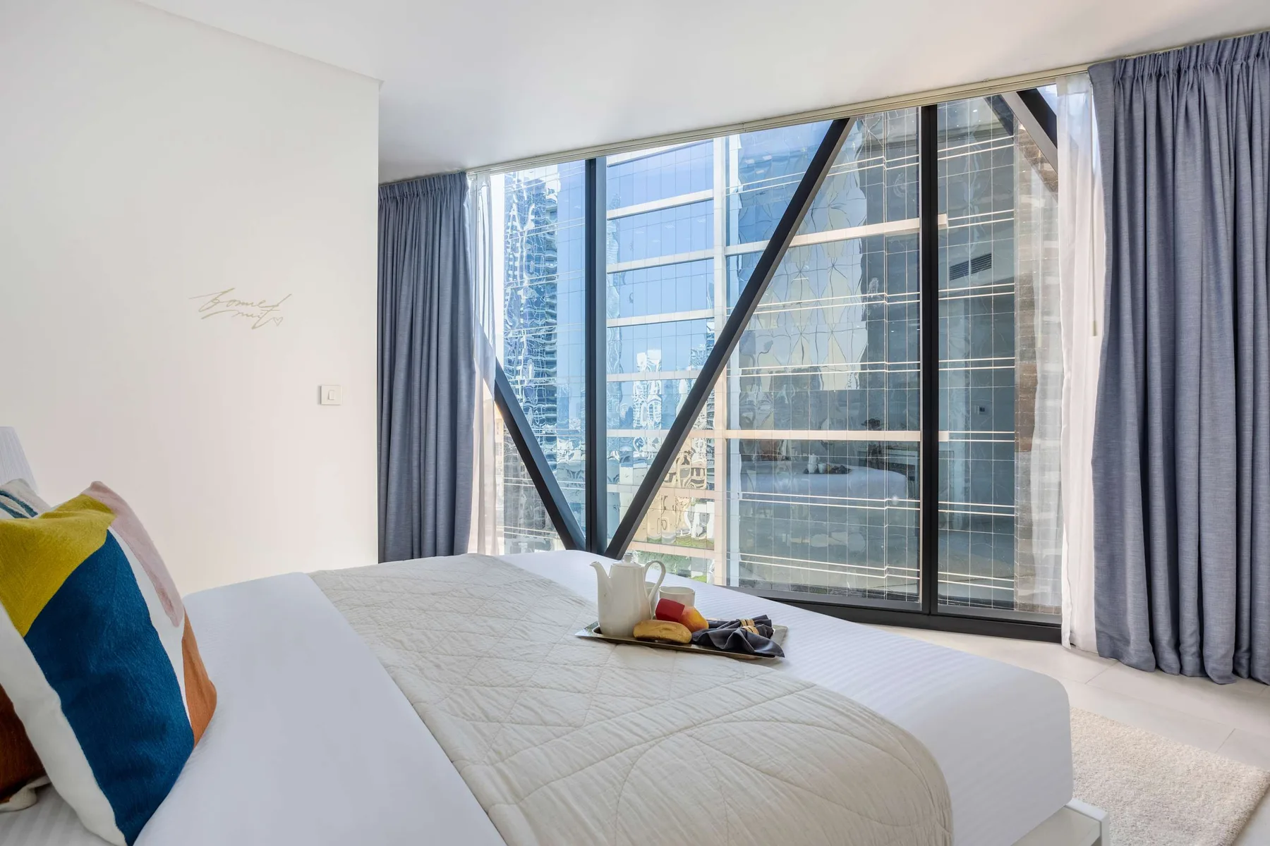 A bedroom with a neatly made bed beside large windows and curtains.