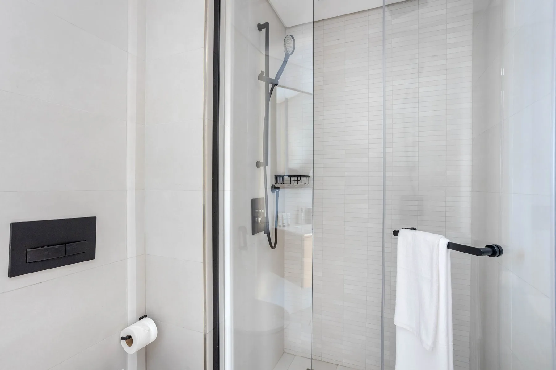 A tiled bathroom with a glass shower and a towel hanging nearby.