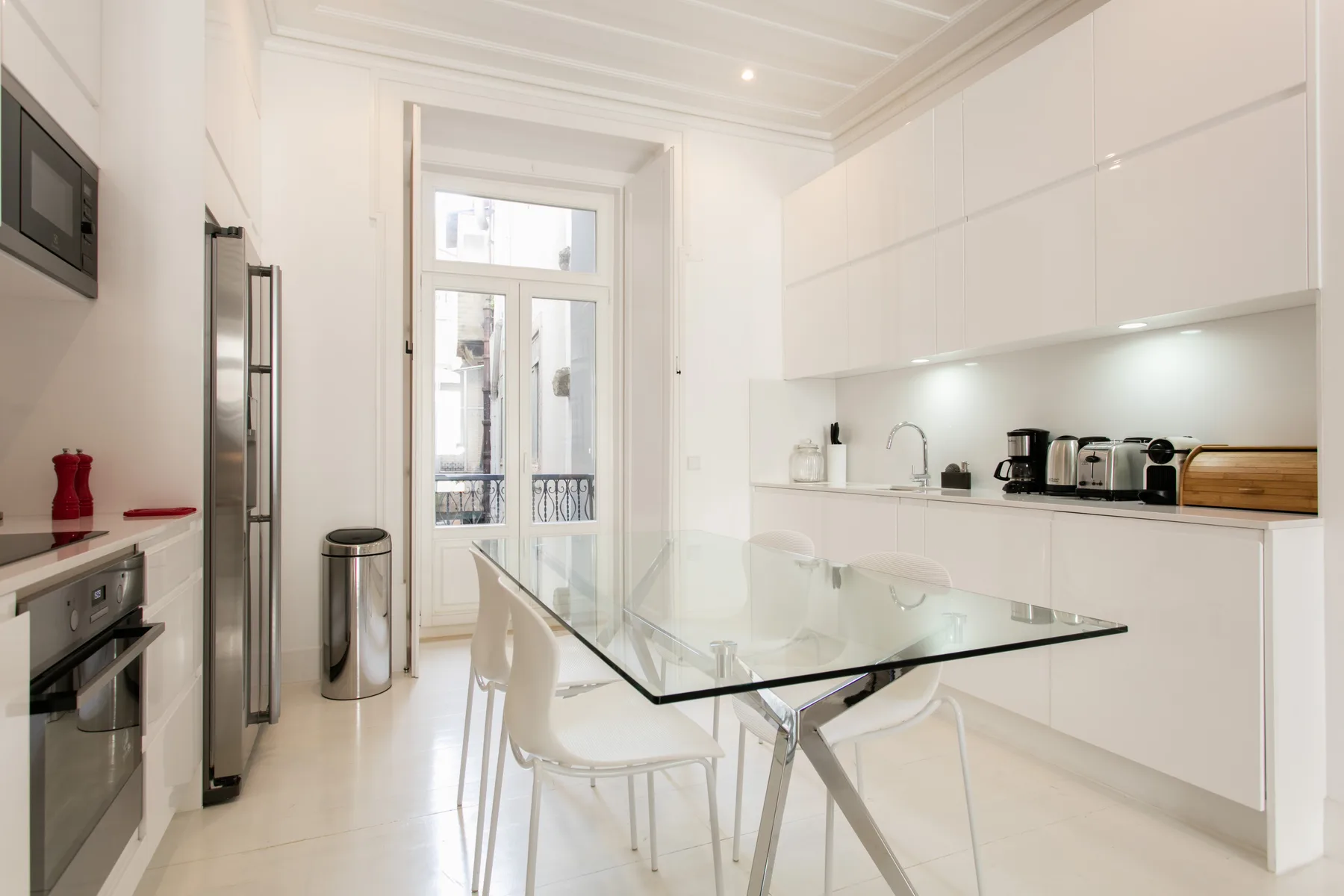 A bright kitchen and dining area with a glass table and white seating.