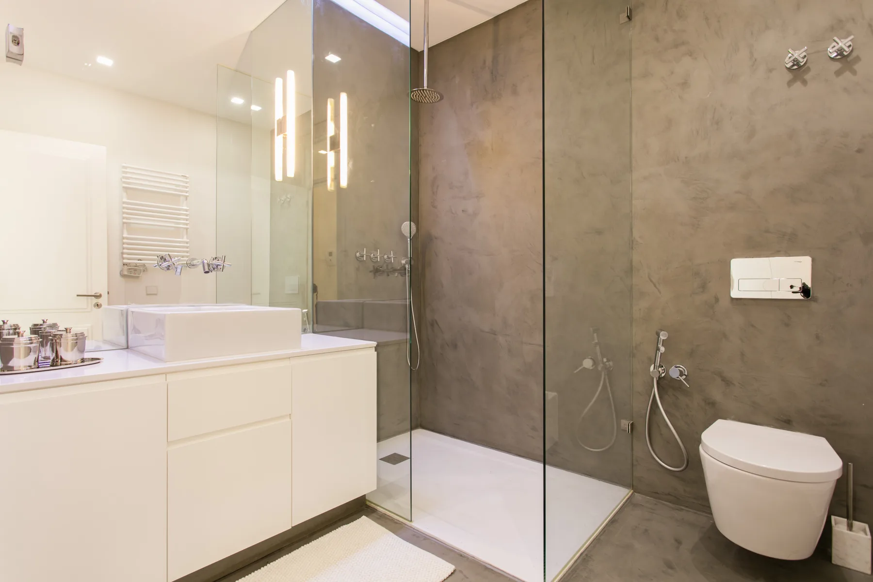 A modern bathroom with a vanity, sink, shower, and wall-mounted toilet.