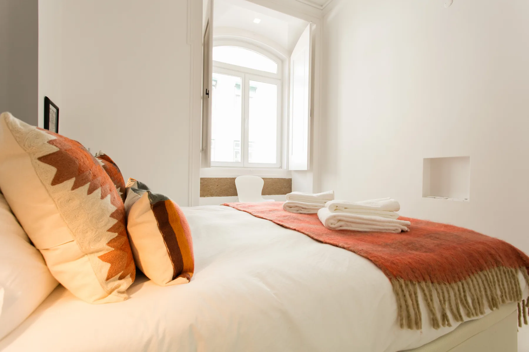 A bright bedroom with a bed, folded towels, and a large arched window.
