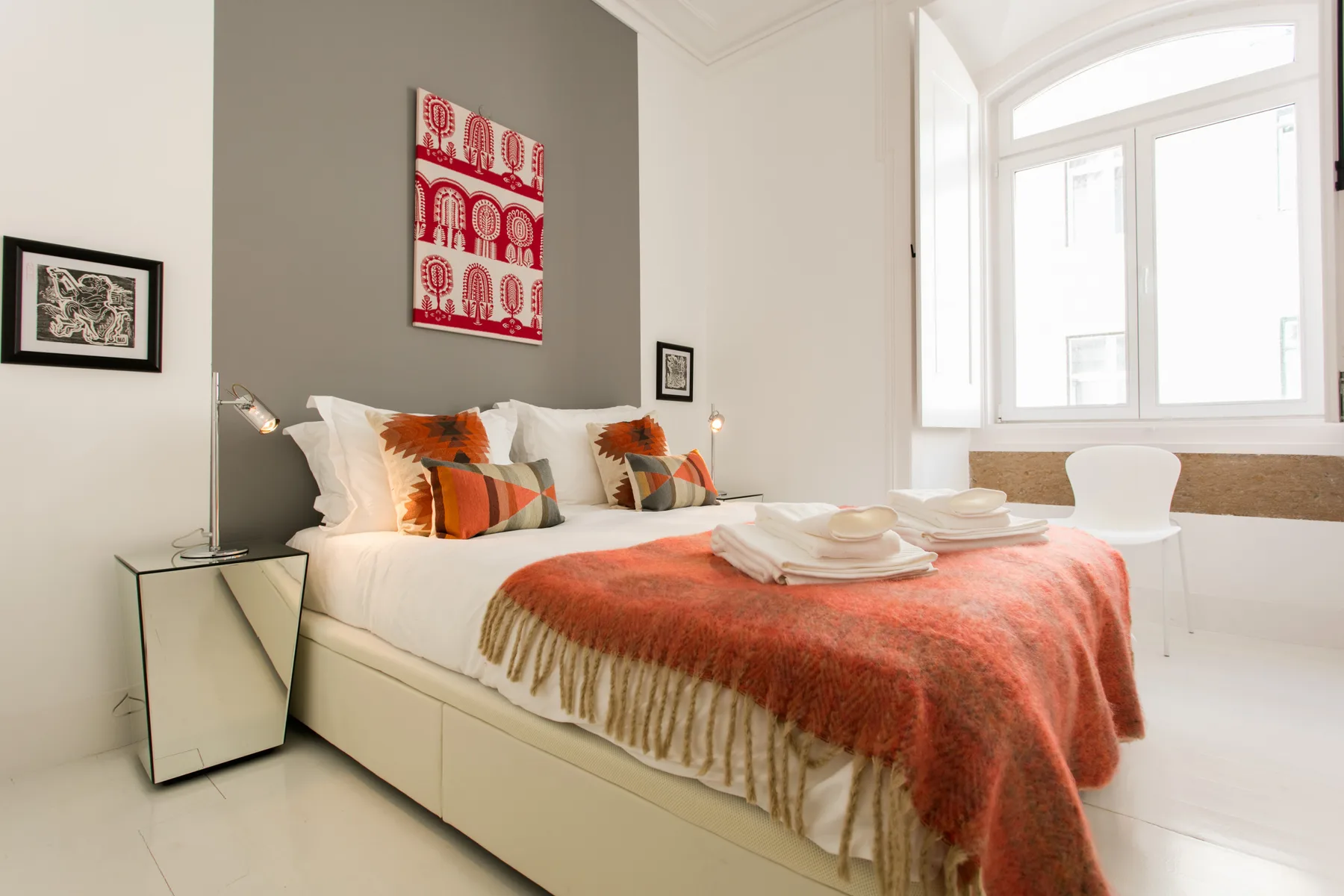 A bedroom with a bed, colorful cushions, and a large window.