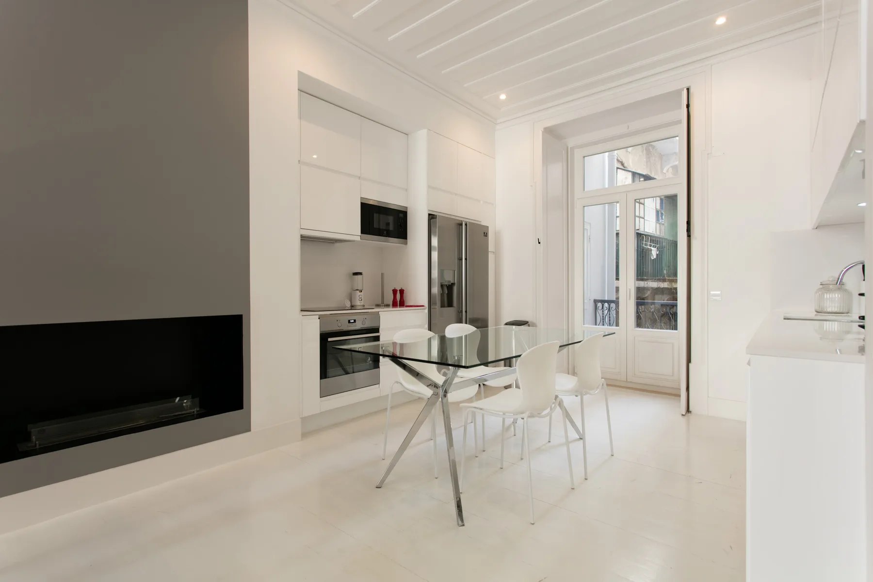 A bright modern kitchen and dining area with a glass table and white seating.
