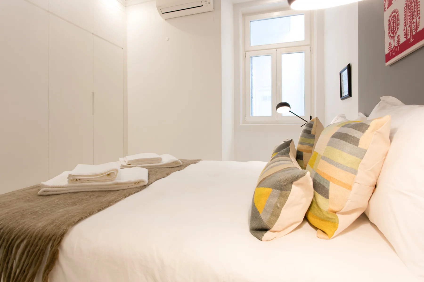A bedroom with a neatly made bed and colorful pillows beside a window.