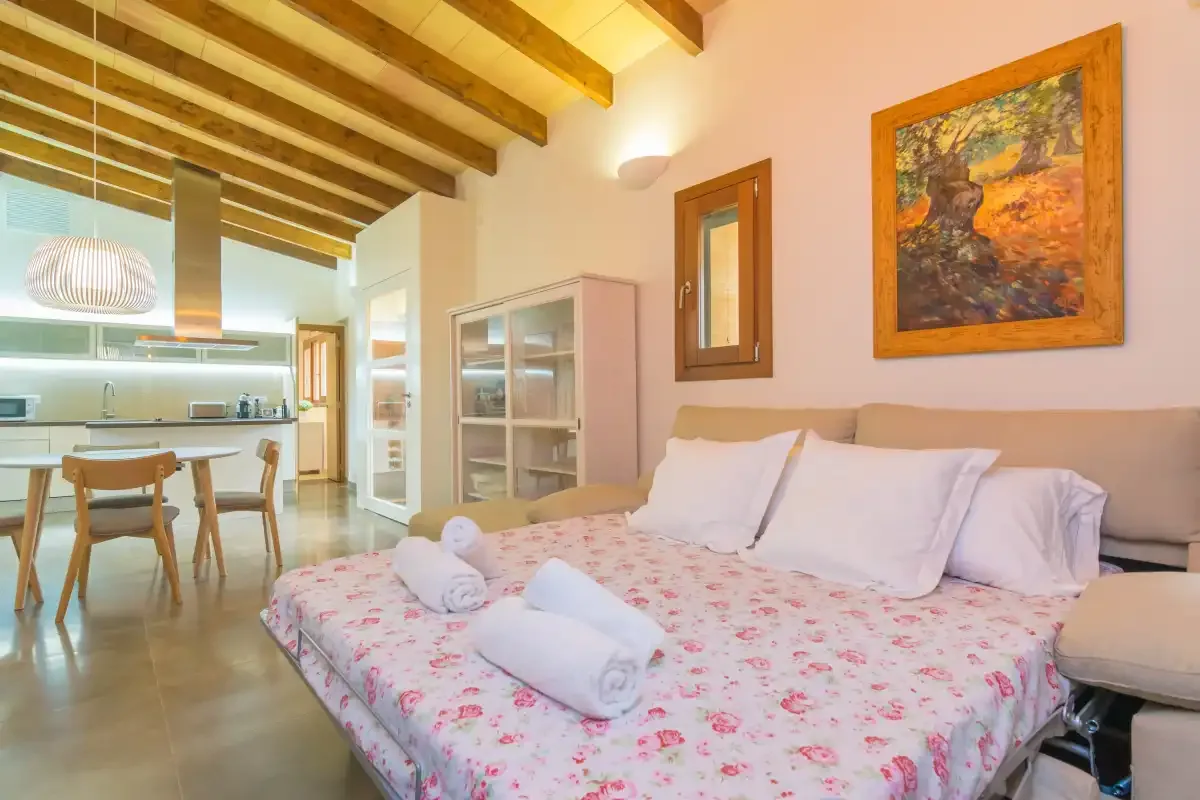 A bedroom with a floral bedspread and an open dining area beyond.