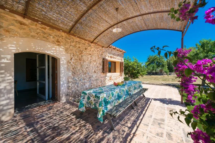 Un patio de piedra con sombra y una mesa bajo un toldo tejido.