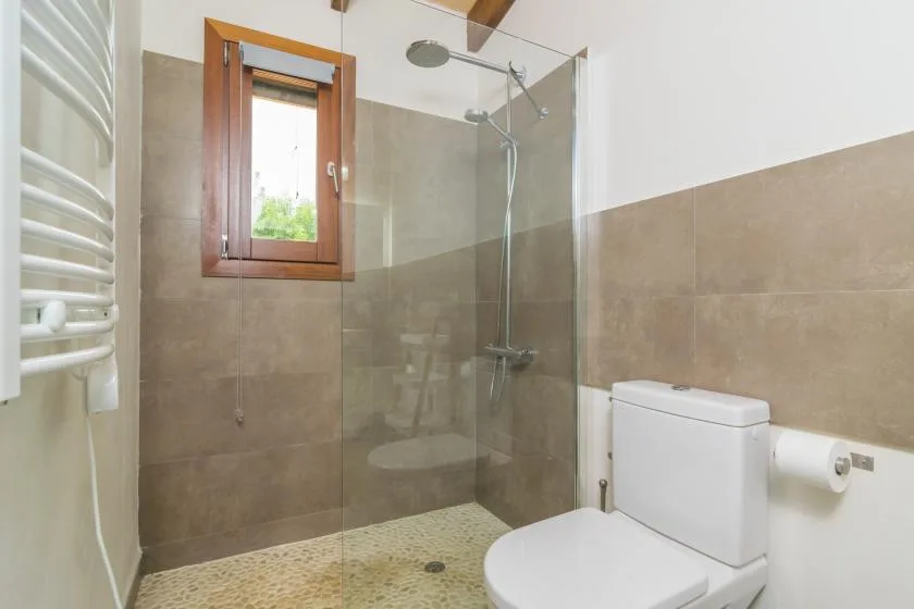 A tiled bathroom with a glass shower, toilet, and small window.