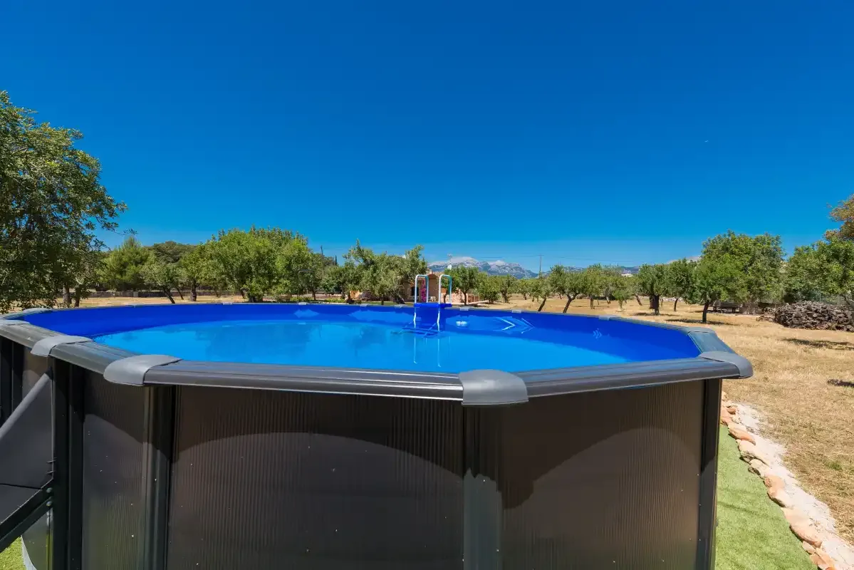 An outdoor above-ground pool sits in a sunny, tree-lined setting.