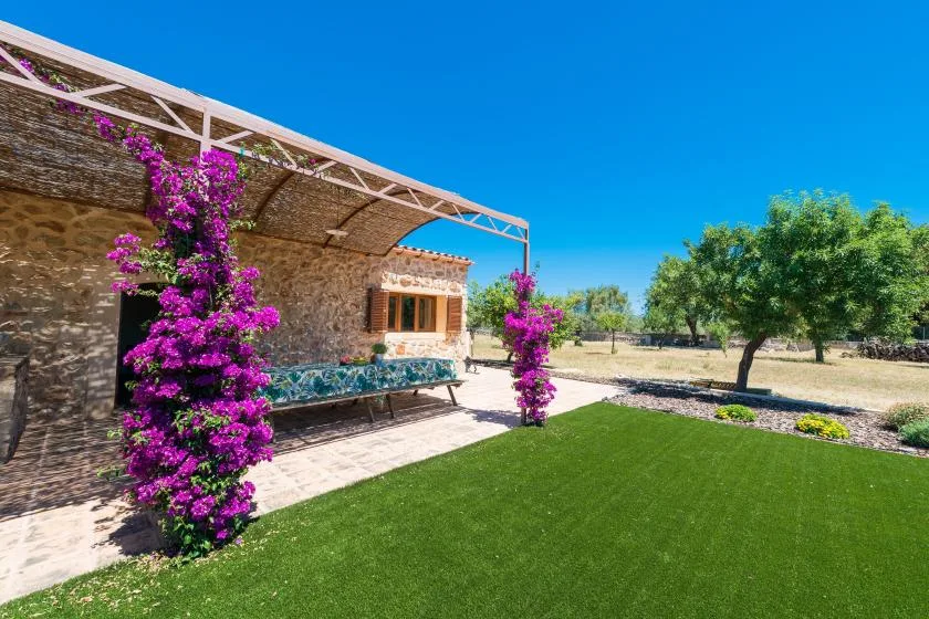 A stone house opens onto a green lawn, with flowering vines beside the patio.