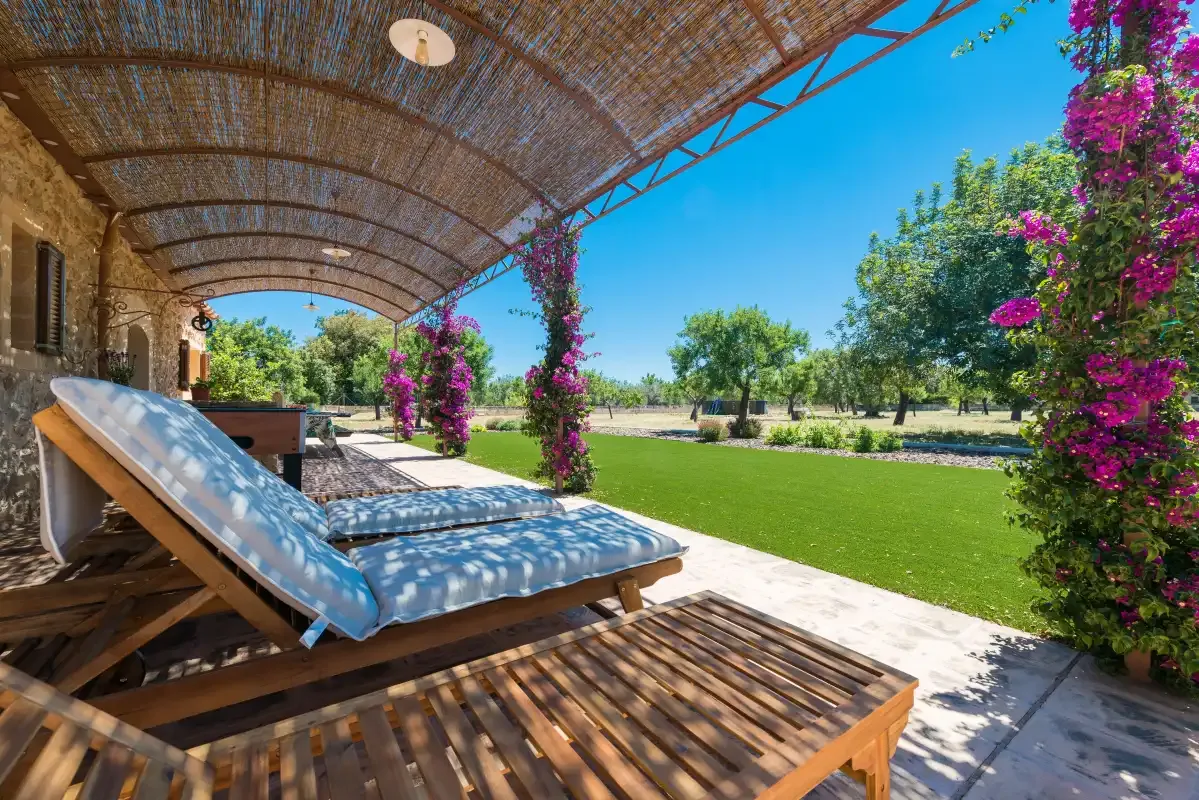 A shaded outdoor patio with lounge seating overlooks a green lawn and trees.