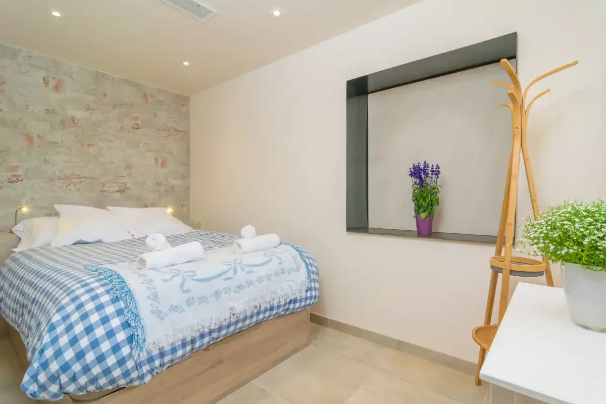 A bedroom with a bed, stone-textured wall, and a potted plant on a shelf.