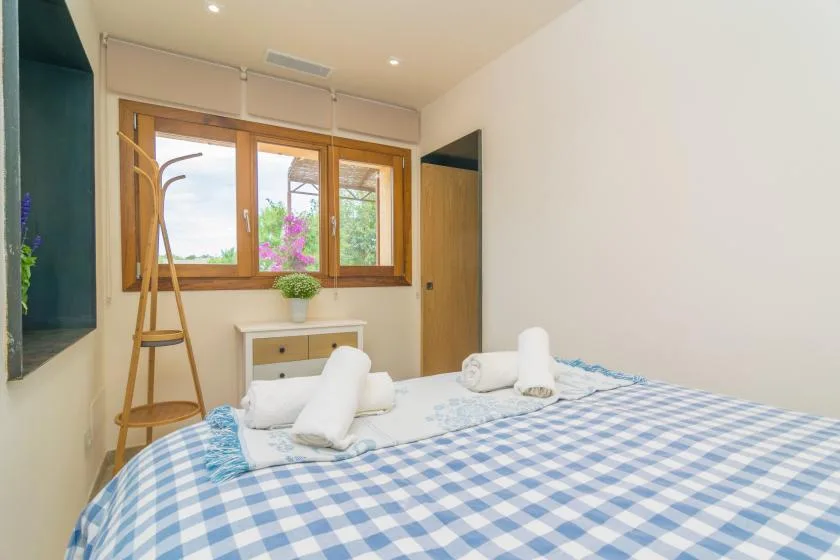 A bedroom with a blue-and-white checked bed beneath a wooden-framed window.