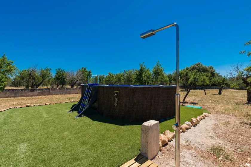 An outdoor pool with a ladder sits beside a grassy yard under a clear blue sky.