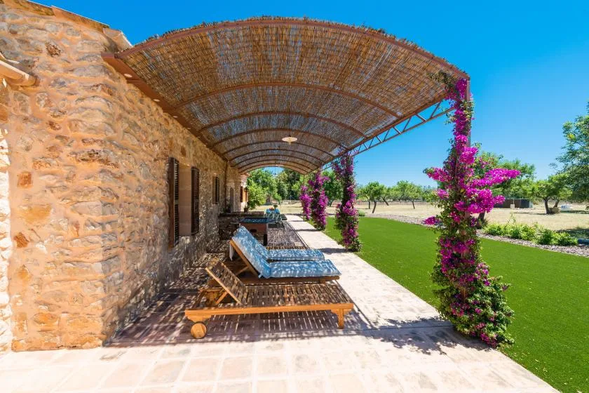 A stone building opens onto a shaded patio with lounge seating and flowering vines.