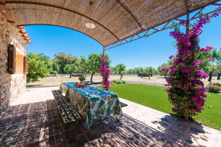 A shaded outdoor dining area overlooks a green lawn and flowering vines.