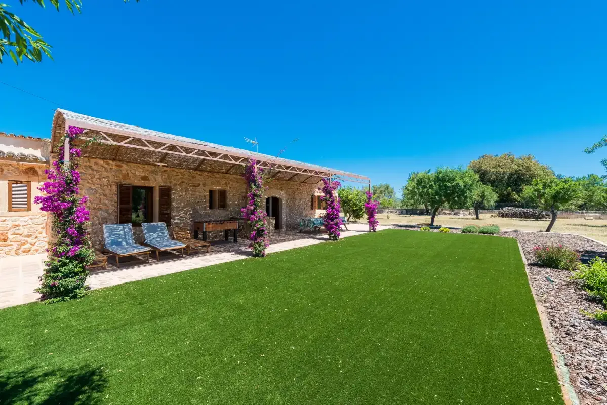 A stone house opens onto a green lawn and a shaded patio.