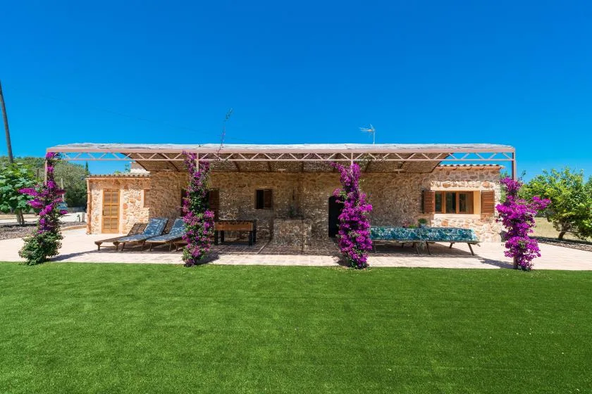 A stone building with a shaded outdoor seating area faces a broad green lawn.
