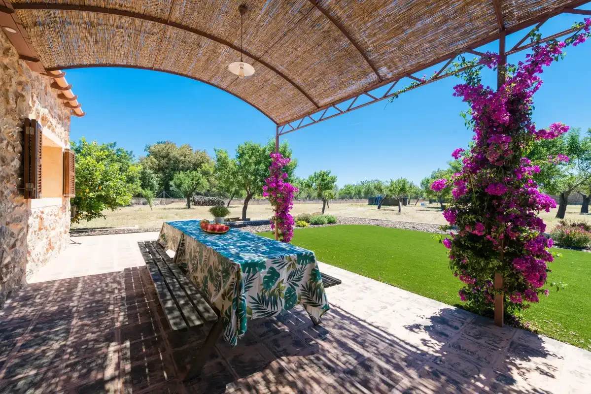 A shaded outdoor dining area opens onto a green lawn and flowering vines.