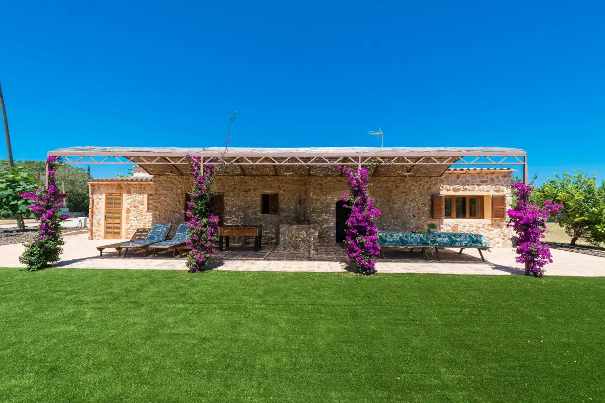 A stone house with a shaded patio and a broad green lawn.