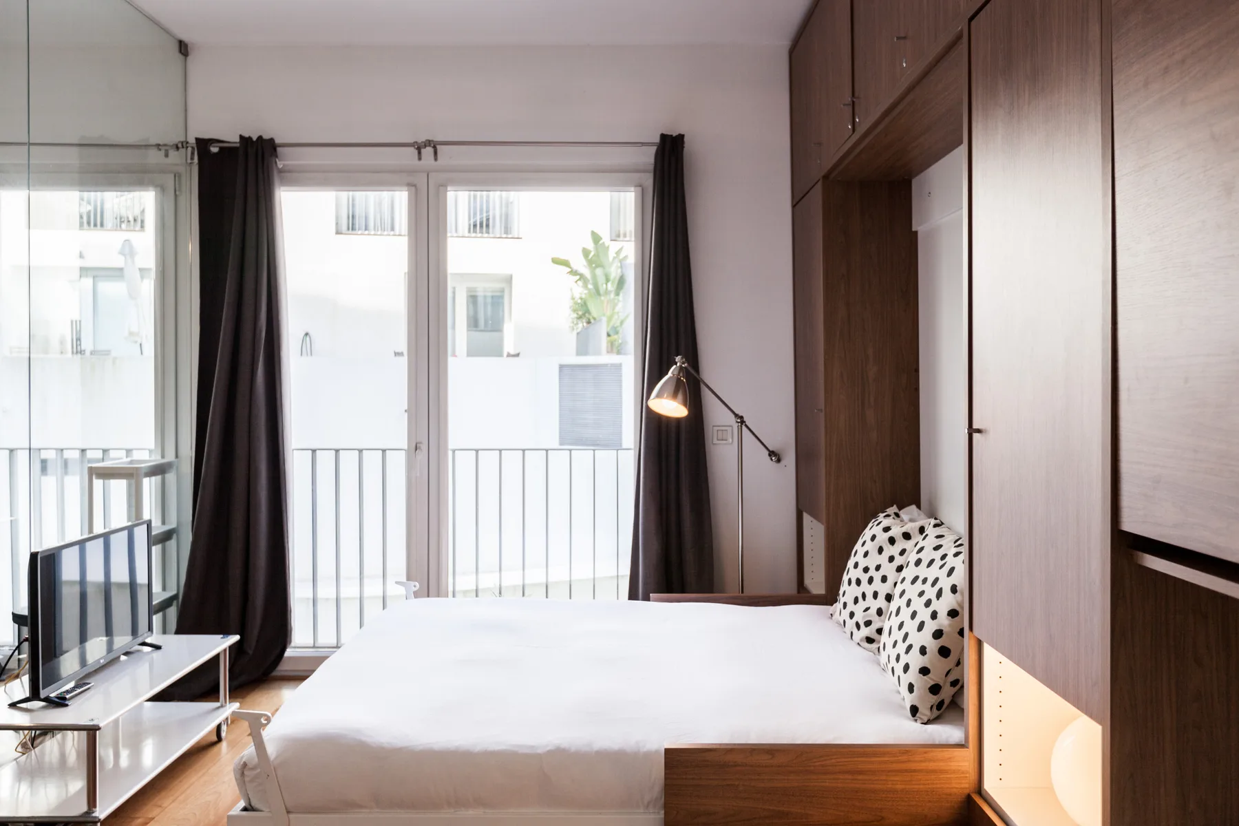 Un dormitorio luminoso con una cama junto a grandes ventanas y armarios empotrados de madera.