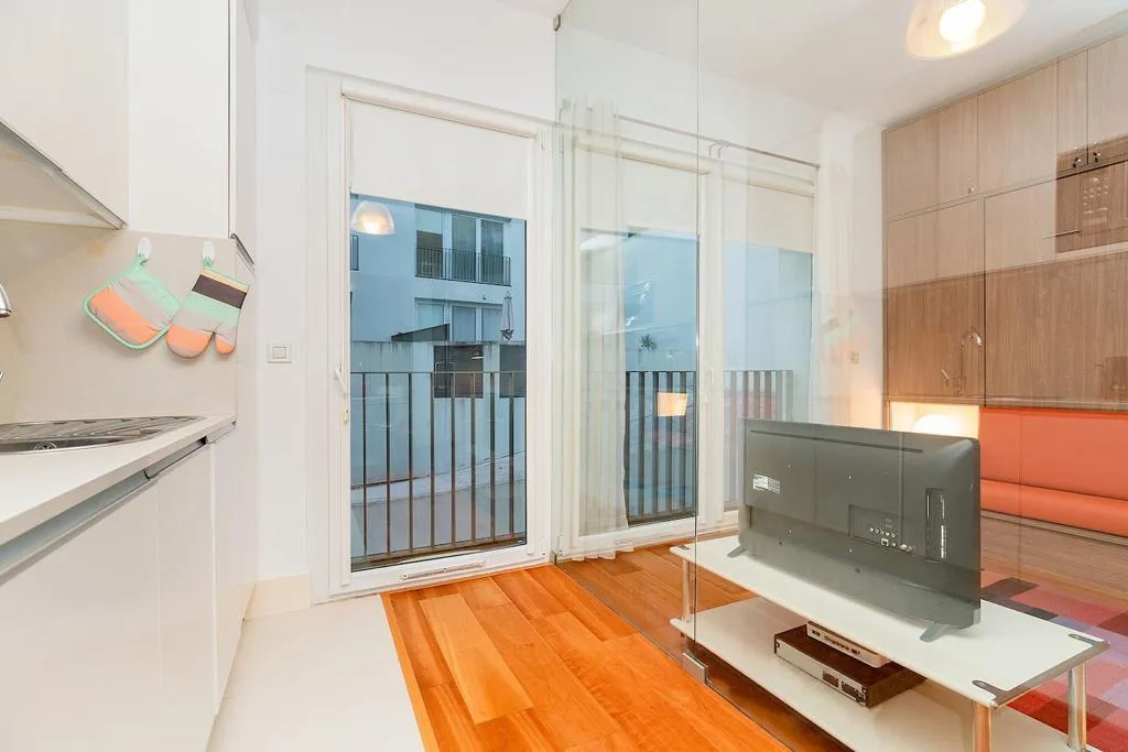 Una luminosa sala de estudio con puertas al balcón, un televisor y asientos naranjas.