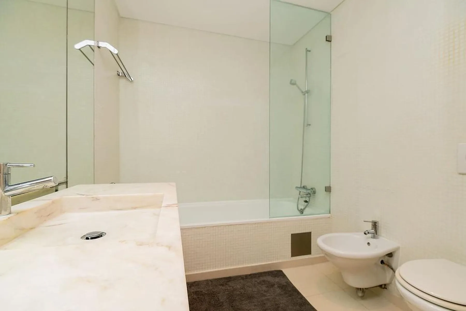 Un baño luminoso con un lavabo largo, bañera y bidé suspendido.