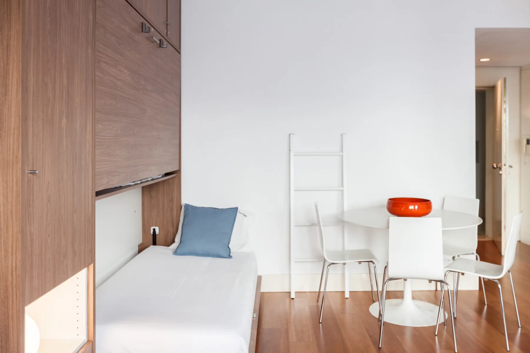 Un estudio luminoso tiene una cama individual junto a una mesa de comedor con sillas.