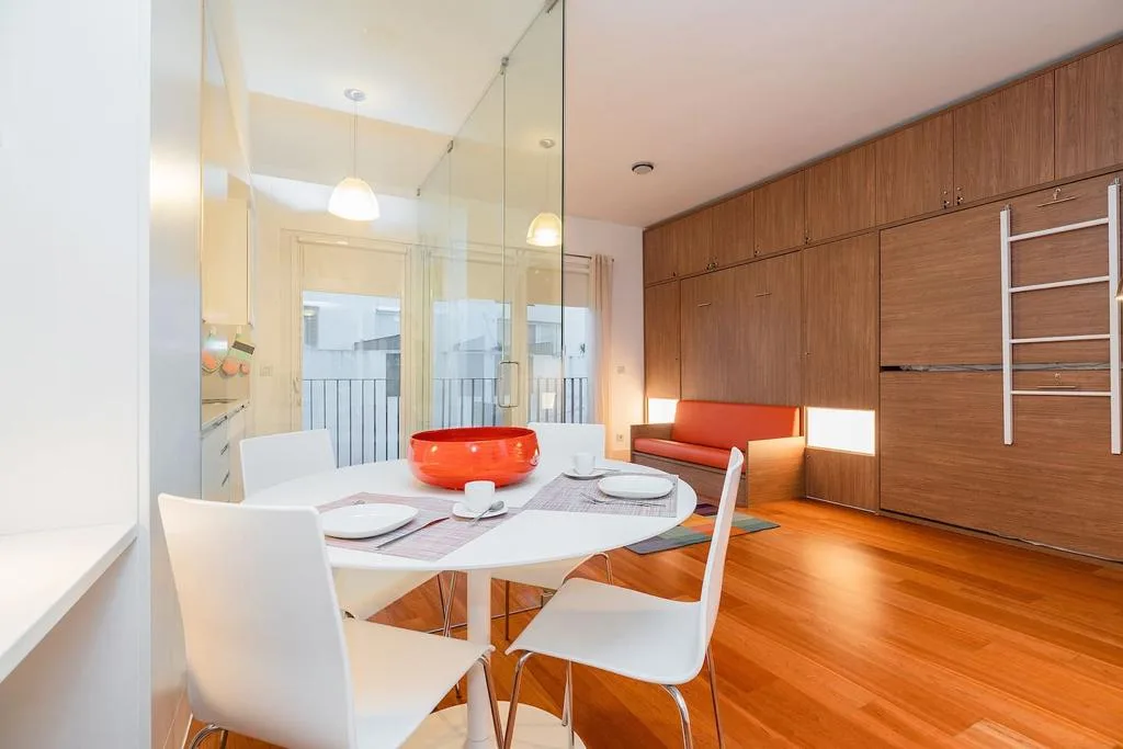 Un comedor luminoso con una mesa blanca junto a una pared revestida de madera.