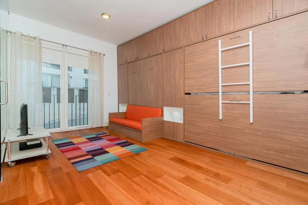Una sala de estar colorida con almacenamiento de madera empotrado y una alfombra llamativa.