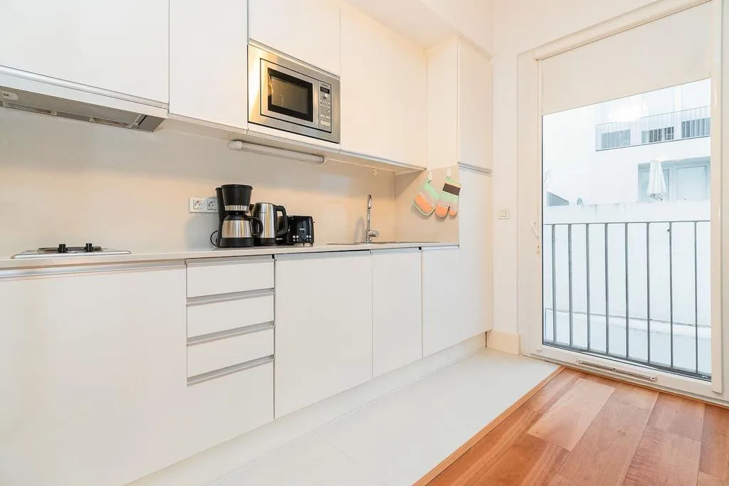 Una cocina luminosa con encimera, armarios y una puerta acristalada al balcón.