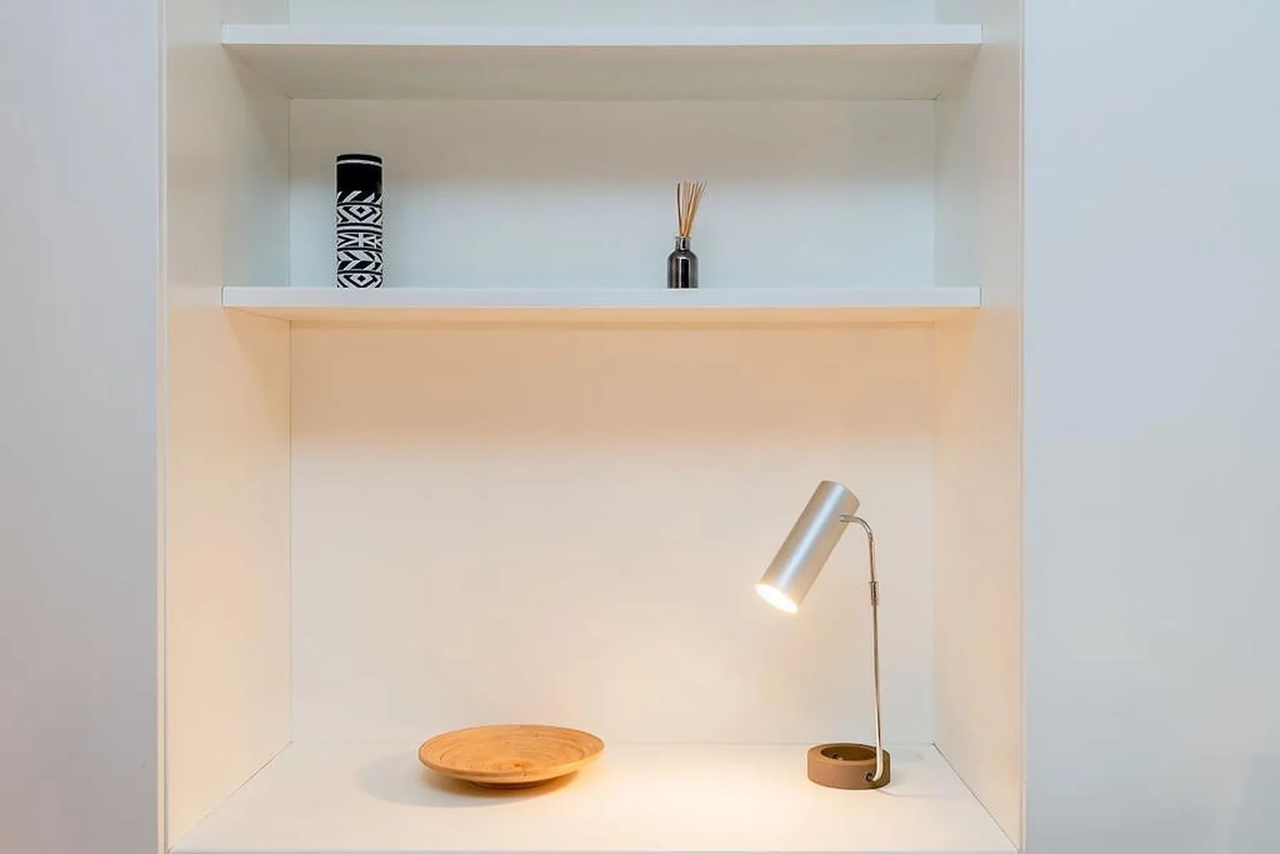 Un estante empotrado muestra una lámpara pequeña, un cuenco de madera y objetos decorativos.