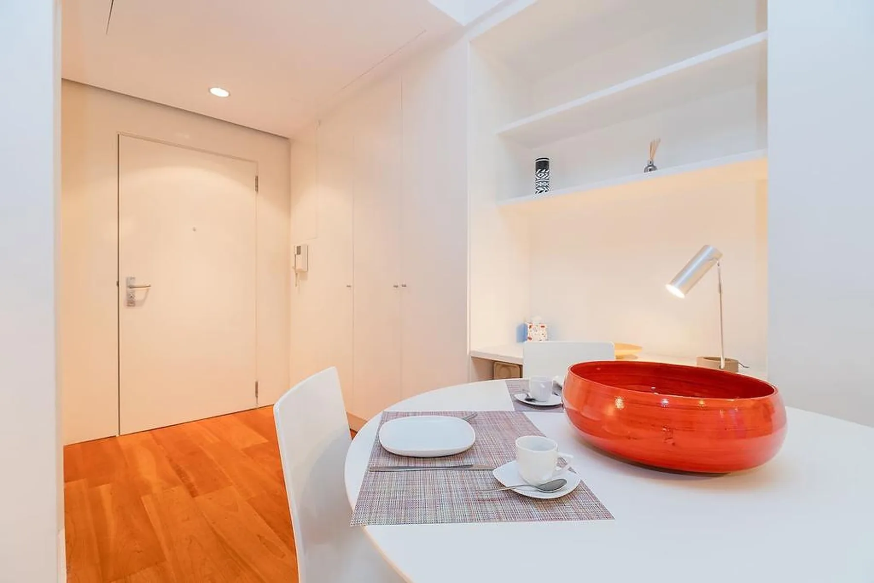 Un comedor luminoso con una mesa preparada con platos junto a estantes empotrados.